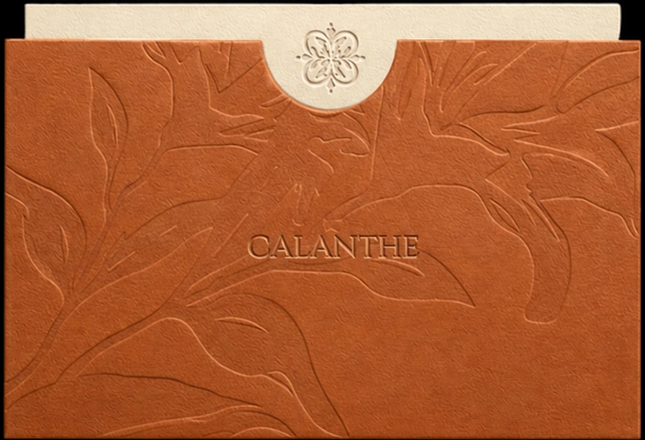 A terracotta Calanthe card, the orchid debossed into the paper, its cream tab pressed with the monogram